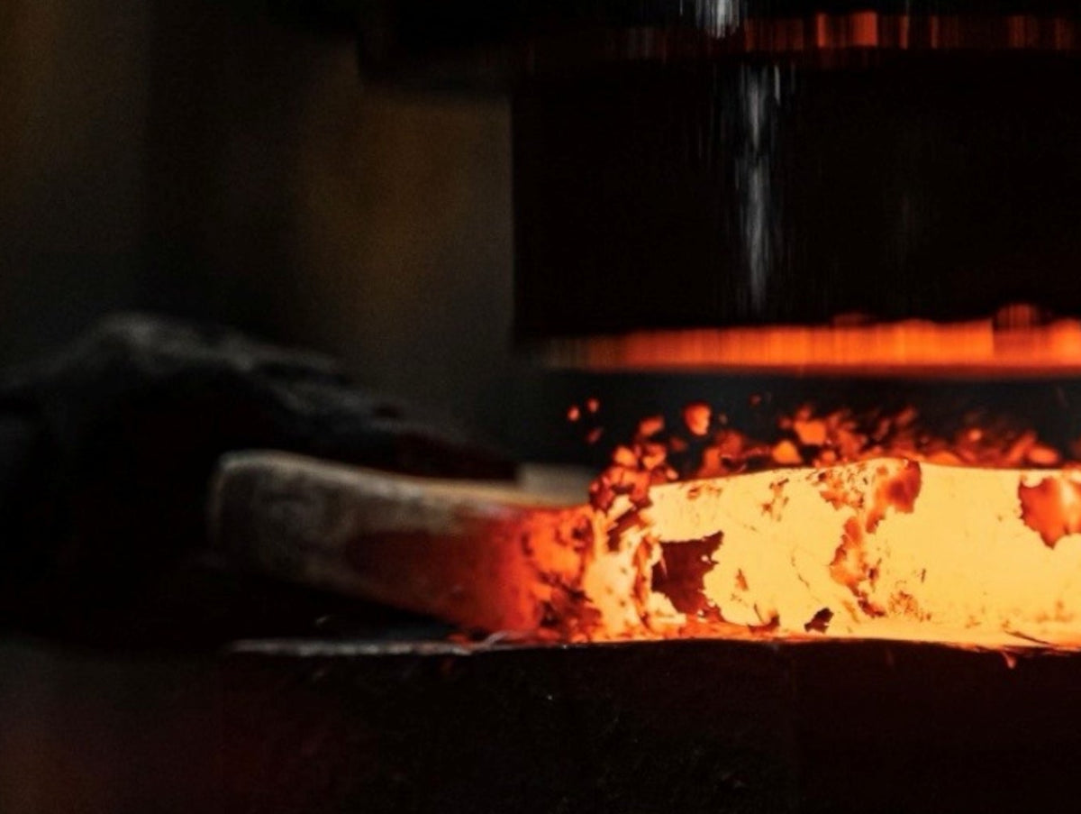 A glowing hot piece of steel being shaped by a heavy industrial press in a blacksmith forge.