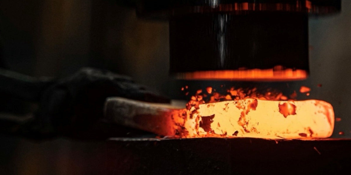 A glowing hot piece of steel being shaped by a heavy industrial press in a blacksmith forge.