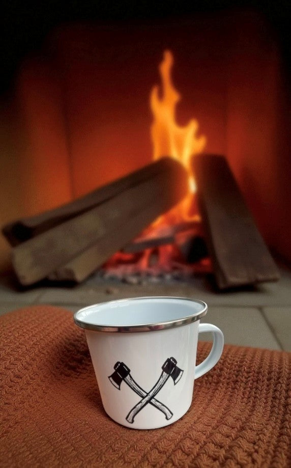 White mug with black design on a brown surface in front of a fireplace.
