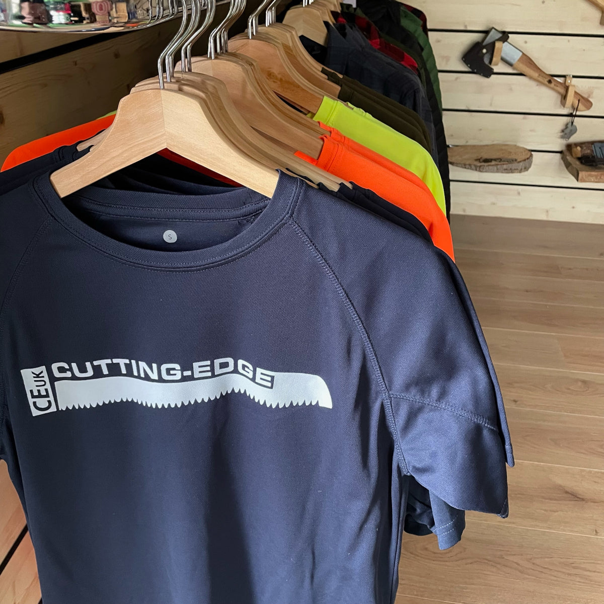 Navy blue t-shirt with 'Cutting Edge' logo on hangers against a wooden wall.