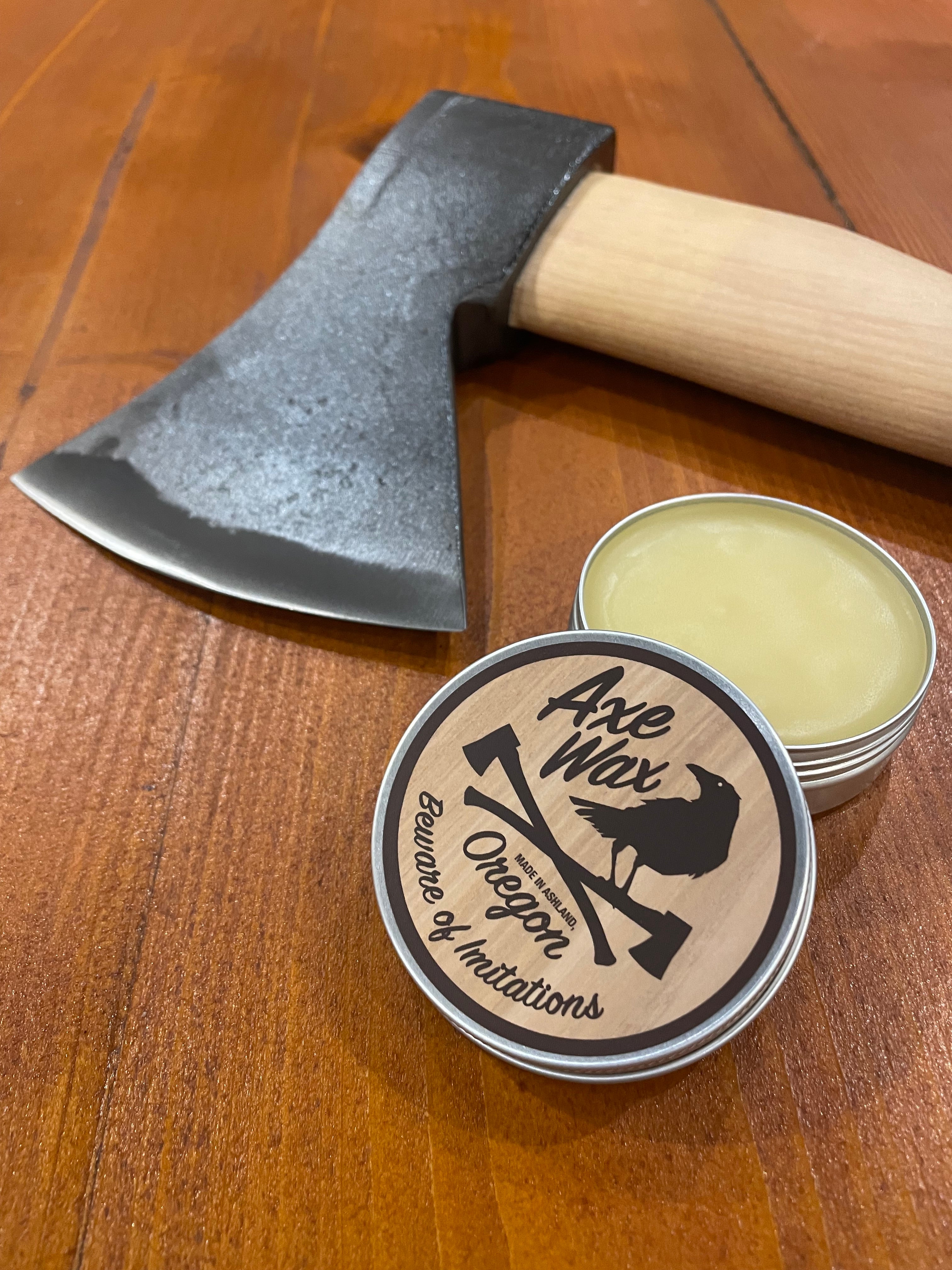 Small tin of wax with a wooden-handled axe on a wooden surface