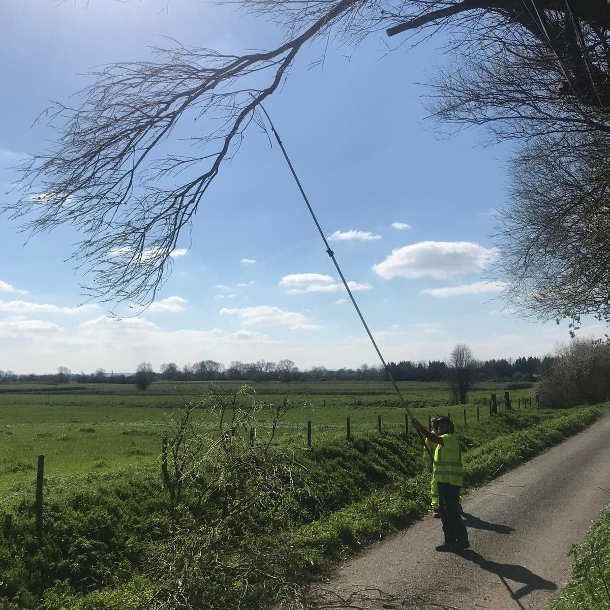 Person on a rural road with a long pole against a clear blue sky