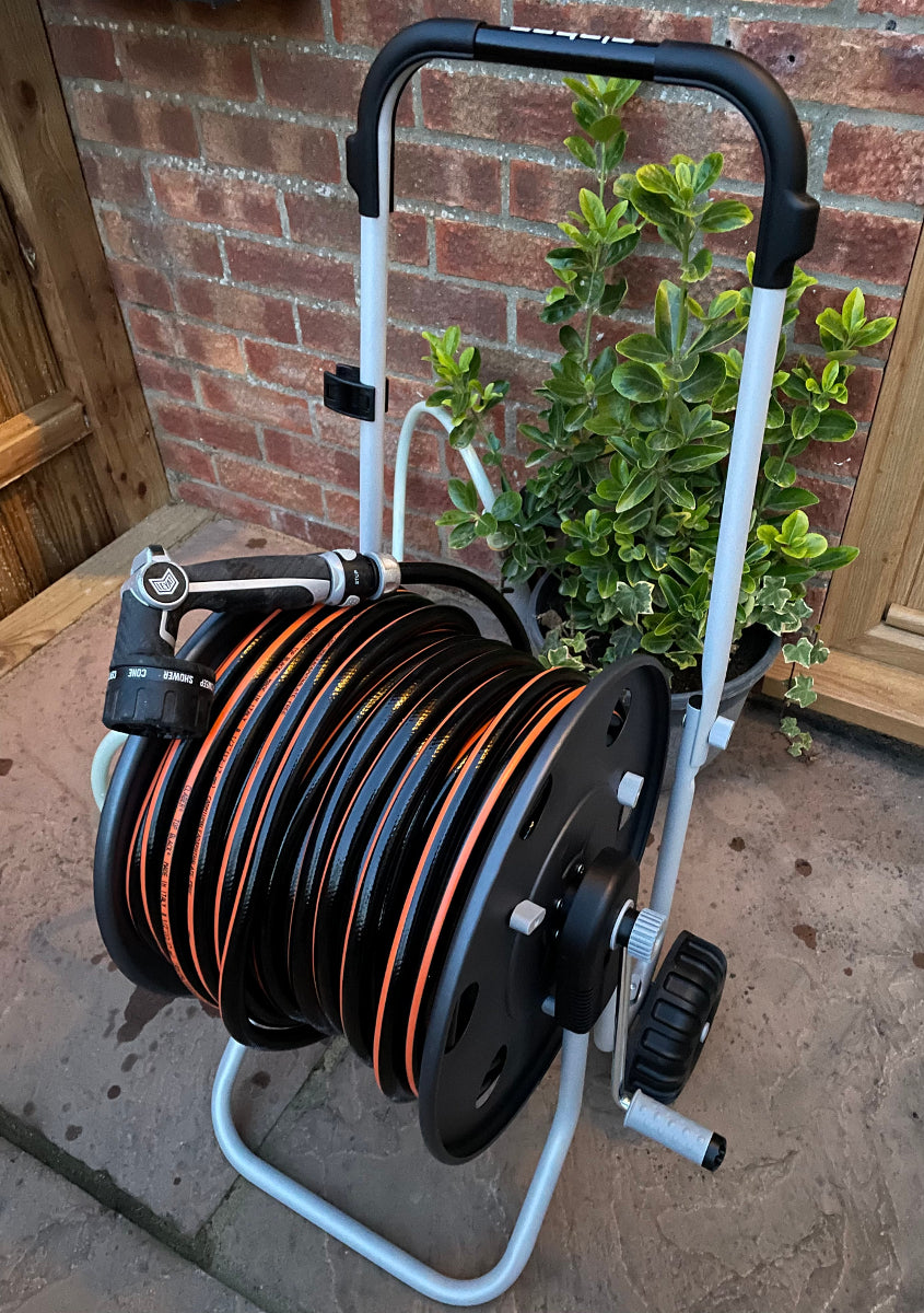 Hose reel cart with hose and plant against a brick wall.